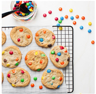 A jar of M&M’s next to a cooling rack of M&M’s cookies.