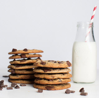 A glass of milk next to two stacks of chocolate chip cookies, a great choice for a cookie dough fundraiser